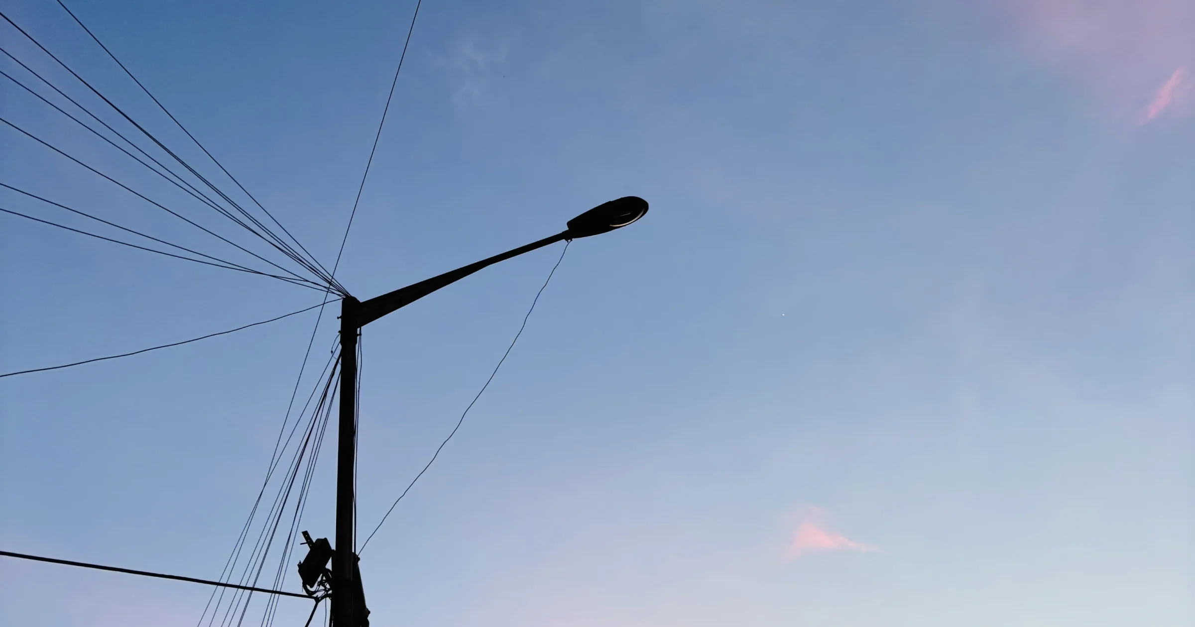 Bengaluru street at night lit by cold white LED streetlights, the road washed out in flat grey-white light with muted buildings and muddled shadows